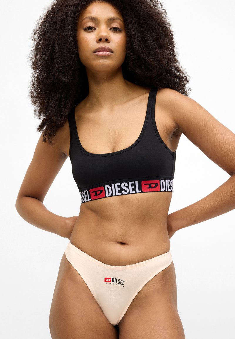Black sports bra with a red and white "DIESEL" logo band; paired with peach-colored thong featuring a small logo print. Soft, snug fit.