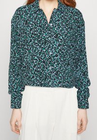Long-sleeve blouse in a blue fabric with a black and green abstract pattern, featuring a classic collar and button-down front detail.