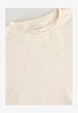 Krémová mikina s rebrovaným výstrihom a svetlým šitím. Obsahuje štítok s textom. Tkanina vyzerá jemne a hladko.