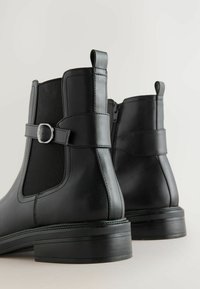Černé kožené kotníkové boty s elastickými bočními panely, bočním zipem a dekorativní přezkou. Hladký povrch a design s vrstvým podpatkem.