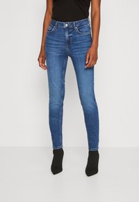 Jeans skinny blu in denim sbiadito con vita alta, dotati di tasche anteriori e cuciture dettagliate. Abbinati a stivali neri alla caviglia.