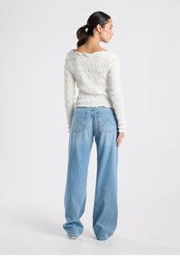 White smocked long-sleeve top with a boat neck, paired with high-waisted light blue wide-leg jeans featuring back pockets.