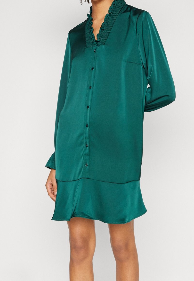 Abito button-up verde in satin con colletto arricciato, maniche lunghe e orlo svasato, dotato di una tasca sul petto.