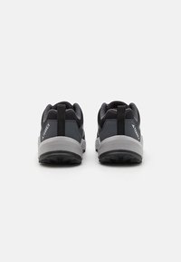 Black athletic shoes with a textured upper, grey outsole, and a pull tab at the heel. Features logo detailing at the sides.