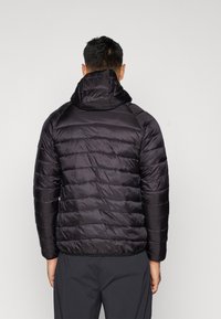 Casaco puffer preto com capuz, apresentando um design acolchoado e uma textura suave. O casaco tem punhos elásticos e uma bainha para uma silhueta justa.