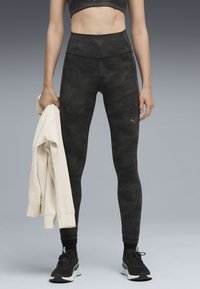 Zwarte leggings met een hoog taille, textuurdesign en logo. Houdt een crèmekleurige sweatshirt vast, draagt zwarte sneakers met muntaccenten.