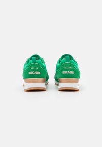 Zapatillas deportivas de ante verde con una entresuela blanca y una suela de goma marrón, que cuentan con un logo en el talón y un collar acolchado.
