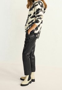 Flødefarvet og sort mønstret fleece-hoodie, sorte læderbukser og cremefarvede ankelstøvler med sorte detaljer. Moderne, afslappet pasform.