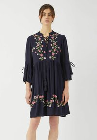 Granatowa sukienka z kwiatowym haftem w odcieniach różu i fioletu. Posiada dekolt w kształcie łezki, dzwonowe rękawy oraz luźną, zwiewną sylwetkę.