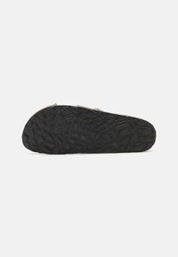 Suola di scarpa in gomma con superficie nera texture, caratterizzata da motivi angolari per aderenza e stabilità. Forma leggermente curvata con bordo rinforzato.
