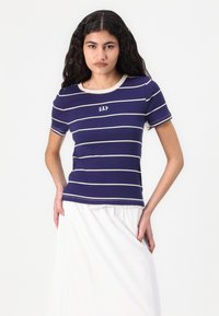 Marineblå stribet t-shirt med beige vandrette striber, rund halsudskæring og "GAP" logo centreret på brystet. Korte ærmer og tætsiddende design.