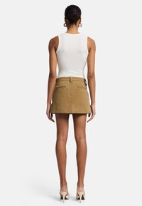 Bruine mini-jurk met een rechte zoom, voorzien van achterzakken en een tailleband. Gecombineerd met een witte geribde tanktop.