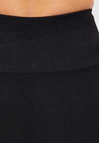 Hochtaillierte schwarze Leggings mit einem gerippten Bund und glatter, matter Textur. V-förmige Nähdetails in der Nähe des unteren Bundes.