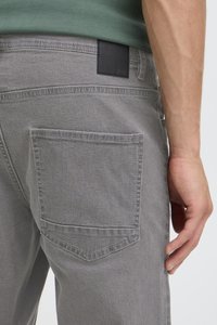 Inimese parema puusa lähivõte, kes kannab halli teksaseid ja rohelist särk, näidates tagataskut ja nähtavat kätt, mis puhkab kõrval.