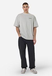 Jasnoszara, oversize koszulka z okrągłym dekoltem i czarnym logo. W połączeniu z czarnymi spodniami typu straight-leg i neutralnymi sneakersami.