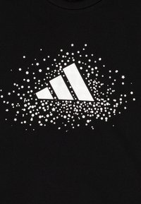 Μαύρη μπλούζα με λογότυπο Adidas σε λευκό, περιτριγυρισμένο από μια έκρηξη από κουκίδες και αστέρια, με απαλή, βαμβακερή υφή.