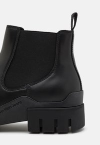 Bottines en cuir noir avec panneau élastique sur les côtés, semelle en caoutchouc texturée et tirant au talon. Présente des coutures audacieuses et un logo.