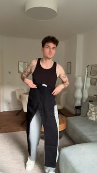 Jeans de mezclilla negros sostenidos, con un diseño clásico de corte recto. La tela parece resistente. El fondo incluye un sofá de color claro y decoración.