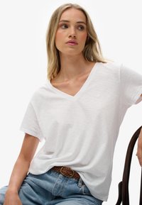 Hvid kortærmet V-hals T-shirt lavet af let stof, kombineret med høj-taljede blå denimjeans og et vævet brunt bælte.