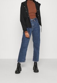 Sort cropped jakke med hætte, ribbet brun turtleneck, blå høj talje jeans og sorte chunk boots. Simpelt design uden mønstre.
