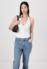 Body blanc sans manches avec un décolleté en V profond, accompagné d'un jean en denim bleu clair taille haute et d'un petit sac à main noir.