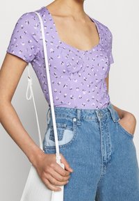 Lila kortärmad topp med fyrkantig halsringning och blommönster; kombinerad med högmidjade blå denimjeans och en vit axelväska.