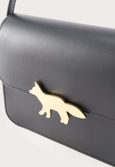 Μαύρη δερμάτινη γυναικεία τσάντα με χρυσή αγκράφα σε σχήμα αλεπούς στο μπροστινό καπάκι και εμφανείς ραφές κατά μήκος των άκρων.