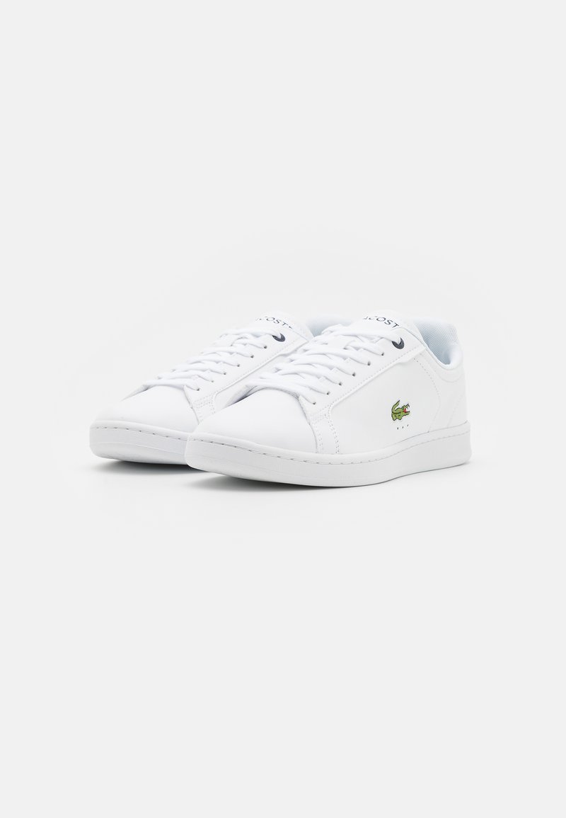 Baskets en cuir blanc avec bout arrondi, lacées à l'avant et logo brodé vert. Texture lisse avec un design minimaliste et des coutures contrastées.