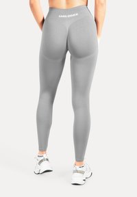 Leggings gris taille haute avec accents texturés et logo à la taille, associés à des chaussures de sport blanches avec détails réfléchissants.