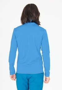 Langærmet, letvægts, lysblå skjorte med en glat tekstur og tætsiddende design, parret med teal bukser. Bagudsigt vist.