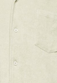 Hellgrünes Hemd mit Knopfleiste aus weichem Stoff, mit einer Tasche auf der linken Seite und zwei Knöpfen, mit einer strukturierten Oberfläche.