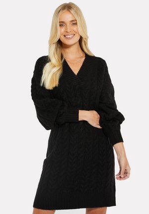 Robe pull en tricot noir avec un décolleté en V, motif chevron texturé, et manches bouffantes avec des poignets et un ourlet côtelés.