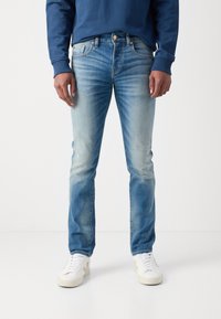 Helle blaue Jeans mit einem ausgewaschenen Finish, Fünf-Taschen-Design, Gürtelschlaufen und geradem Bein. Kombiniert mit weißen Schuhen.