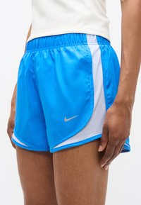 Modre športne kratke hlače iz gladkega materiala z belim mrežastim poudarkom, zrebrnim logotipom na strani in elastičnim pasom.