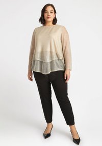 Top a strati beige chiaro con maniche lunghe in chiffon e intricati motivi floreali, abbinato a pantaloni neri slim-fit e scarpe nere a punta.