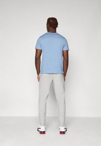 Lyseblå T-shirt med korte ærmer og et subtilt mønster, parret med lysegrå sweatpants og hvide sneakers med røde accenter.