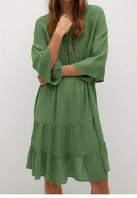 Abito verde a più livelli con finitura testurizzata, caratterizzato da un collo rotondo, dettaglio a chiave aperta e maniche larghe. Realizzato in tessuto leggero.