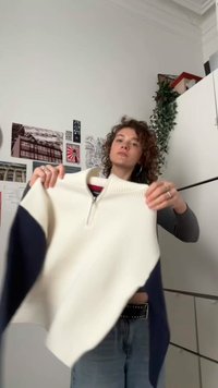 Witte geribbelde gebreide trui met marineblauwe accenten, met een hoge kraag en een ritssluiting aan de voorkant. De mouwen hebben een kleurblokontwerp.