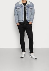 Jeansjacka med fårskinnskrage, svart t-shirt, svarta slim-fit byxor och grå sportskor med svarta detaljer.