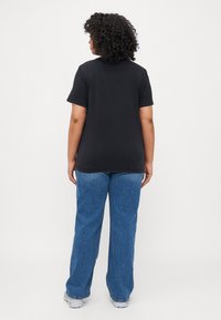 Svart bomulls t-skjorte med korte ermer, parret med lyseblå vide denimjeans. Dette antrekket har en avslappet passform og glatt tekstur.