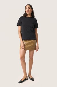 Tricou din bumbac negru, cu mâneci scurte, asociat cu o fustă mini din piele maro, cu o textură netedă. Pantofii negri cu vârf ascuțit completează aspectul.