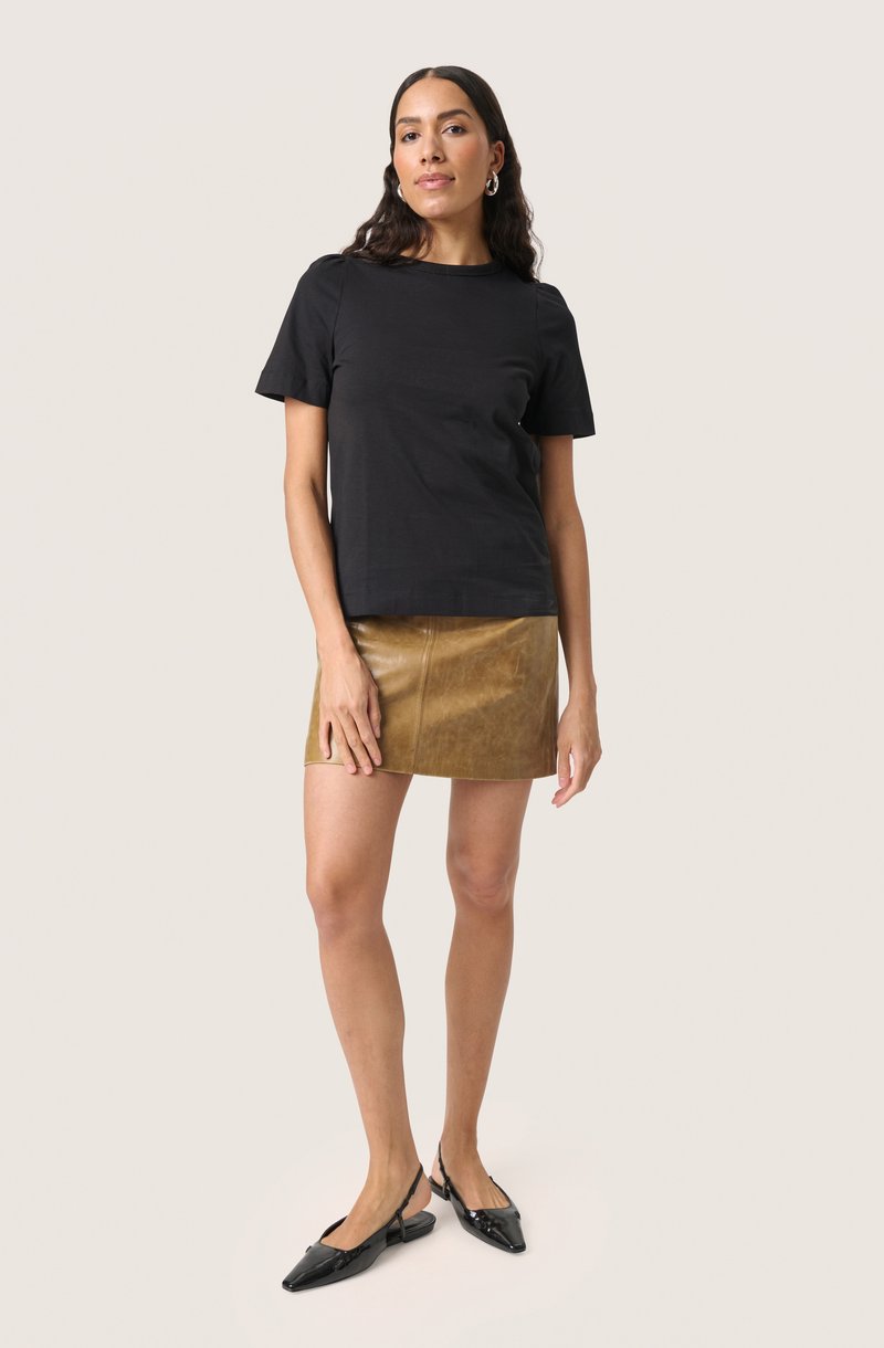 T-shirt in cotone nero, maniche corte, abbinato a una mini gonna in pelle marrone, con una texture liscia. Aperta il look con delle ballerine nere a punta.
