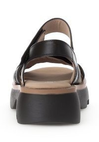 Czarna sandał z syntetyczną cholewką, wieloma paskami, wypchaną beżową wkładką i grubą czarną podeszwą platformową. Widok od tyłu.