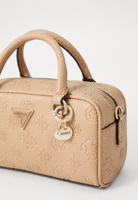 Borsa in tessuto beige con manici doppi e finiture dorate. Presenta motivi con logo impresso e chiusura con cerniera. Include un portachiavi decorativo.