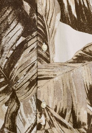 Barna és bézs trópusi leveles mintázat szöveten, két fehér gombbal, amelyek egy varrás mentén láthatóak.