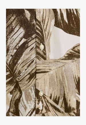 Brunt og beige tropisk løvverkmønster på stoff med to hvite knapper synlige langs en søm.