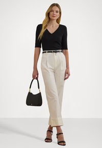 Zwarte V-hals top, hooggetailleerde crèmekleurige broek met plooien, zwarte riem en een zwarte handtas. Sleehak sandalen met banden in het zwart, gladde texturen.