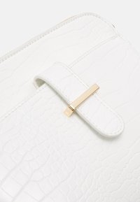 Borsa in pelle bianca con motivo a coccodrillo testurizzato, dotata di una chiusura con fermaglio in oro e una tracolla liscia per la chiusura.