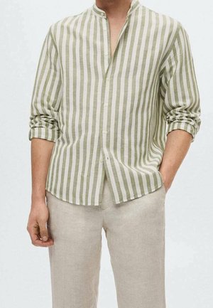 Hombre con pantalones de lino beige claro y camisa de manga larga a rayas verticales verdes y blancas con las mangas remangadas.