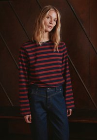 Tumesinised ja punased triibulised pika varrukaga särgid koos tumedate teksapükstega; särgil on ümar kaelus ja vaba lõige.